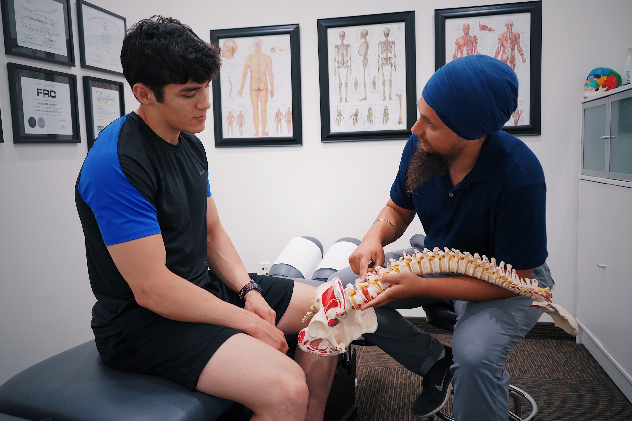 A practitioner holding a model of the spine while he explains a diagnosis to a young man