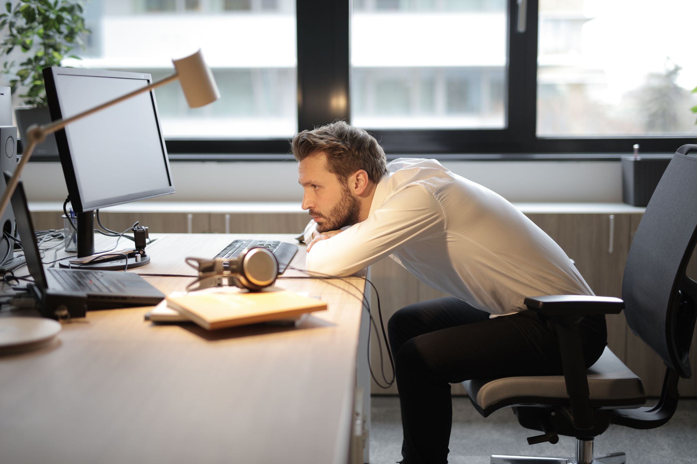 A man slumped forward at his office desk with a sore back
