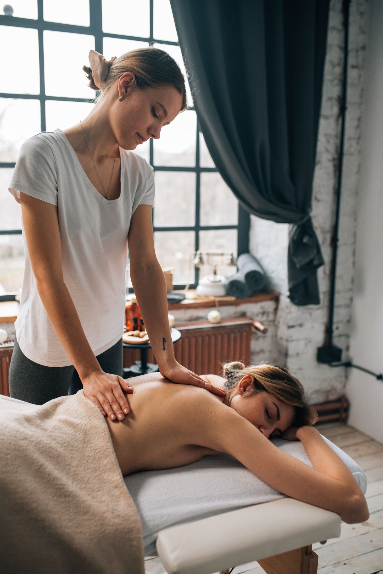 A massage therapist working on a client's back in a bright room with large windows