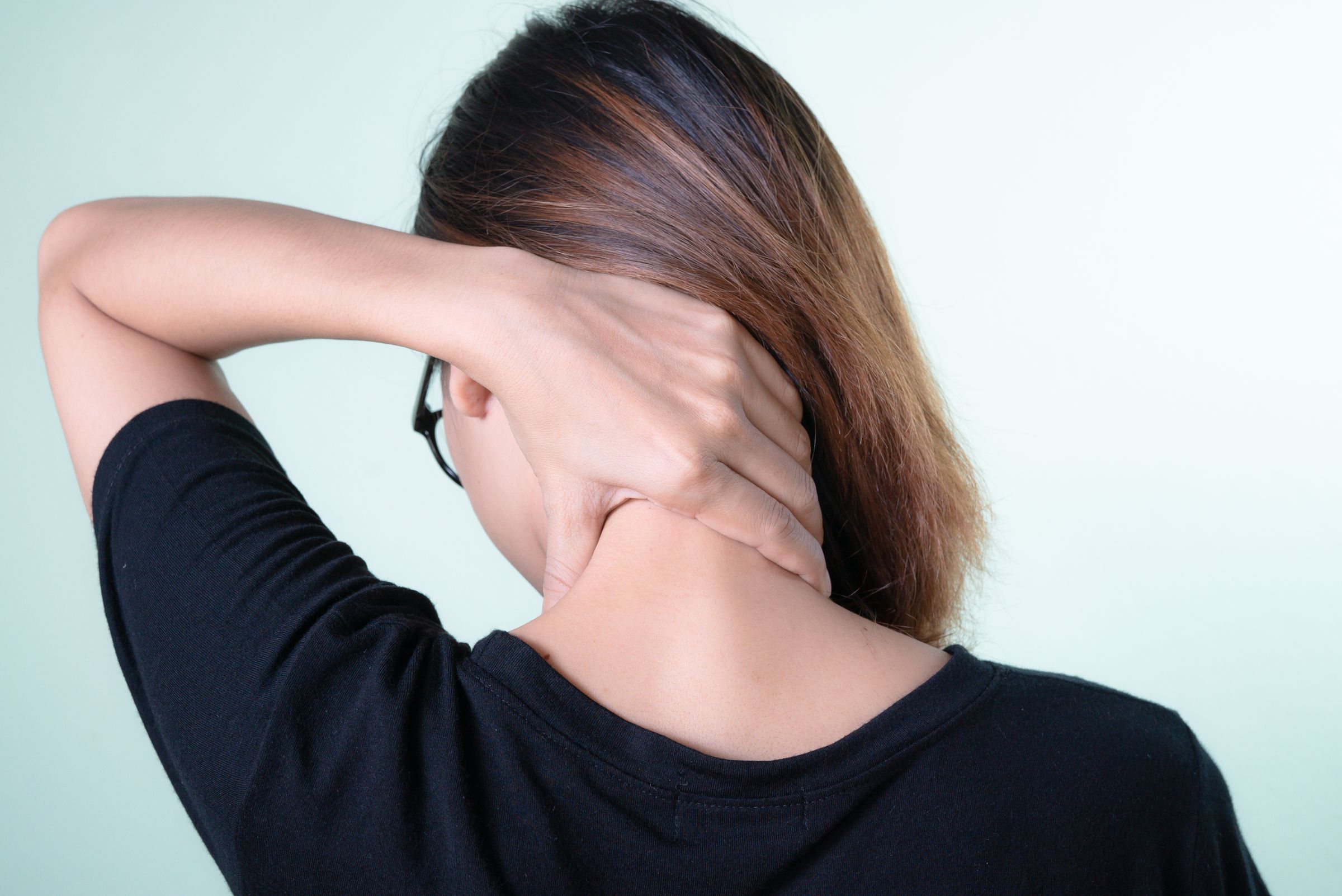 A woman seen from behind, holding the back of her sore neck