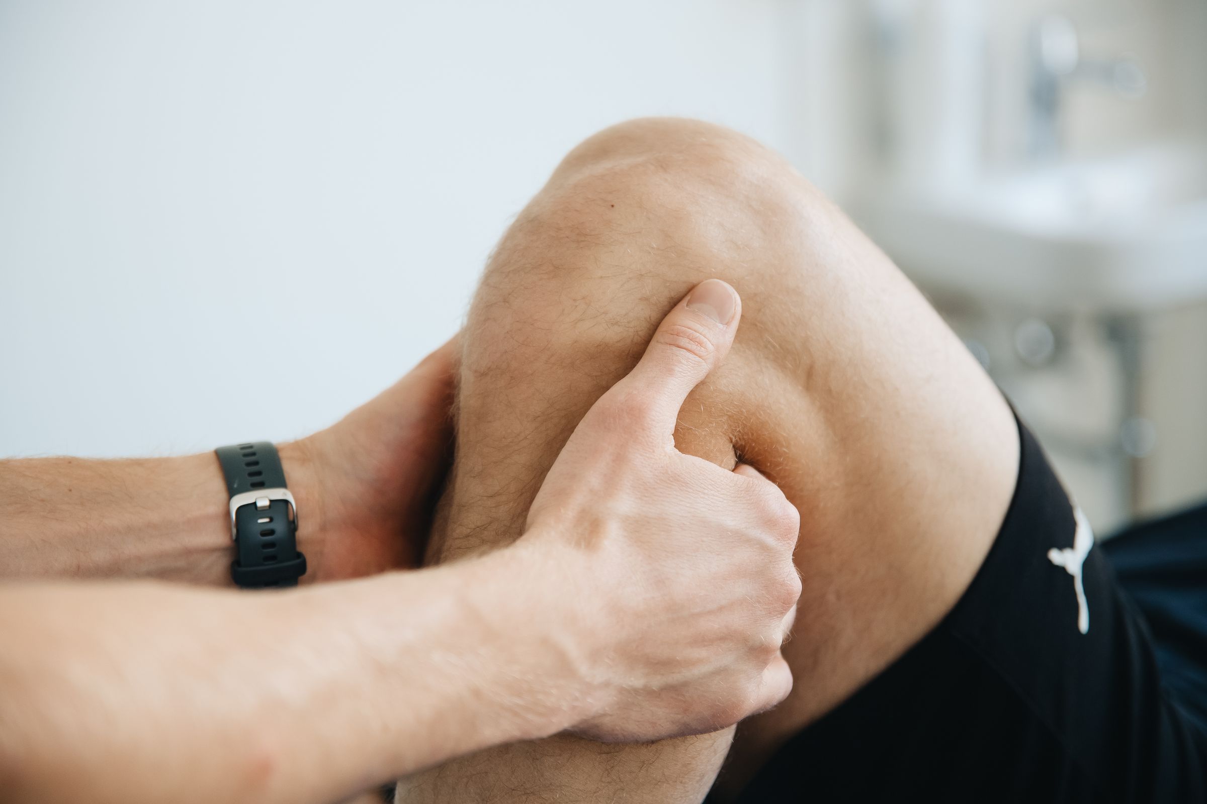 A therapist's hands working on the muscles around a patient's knee