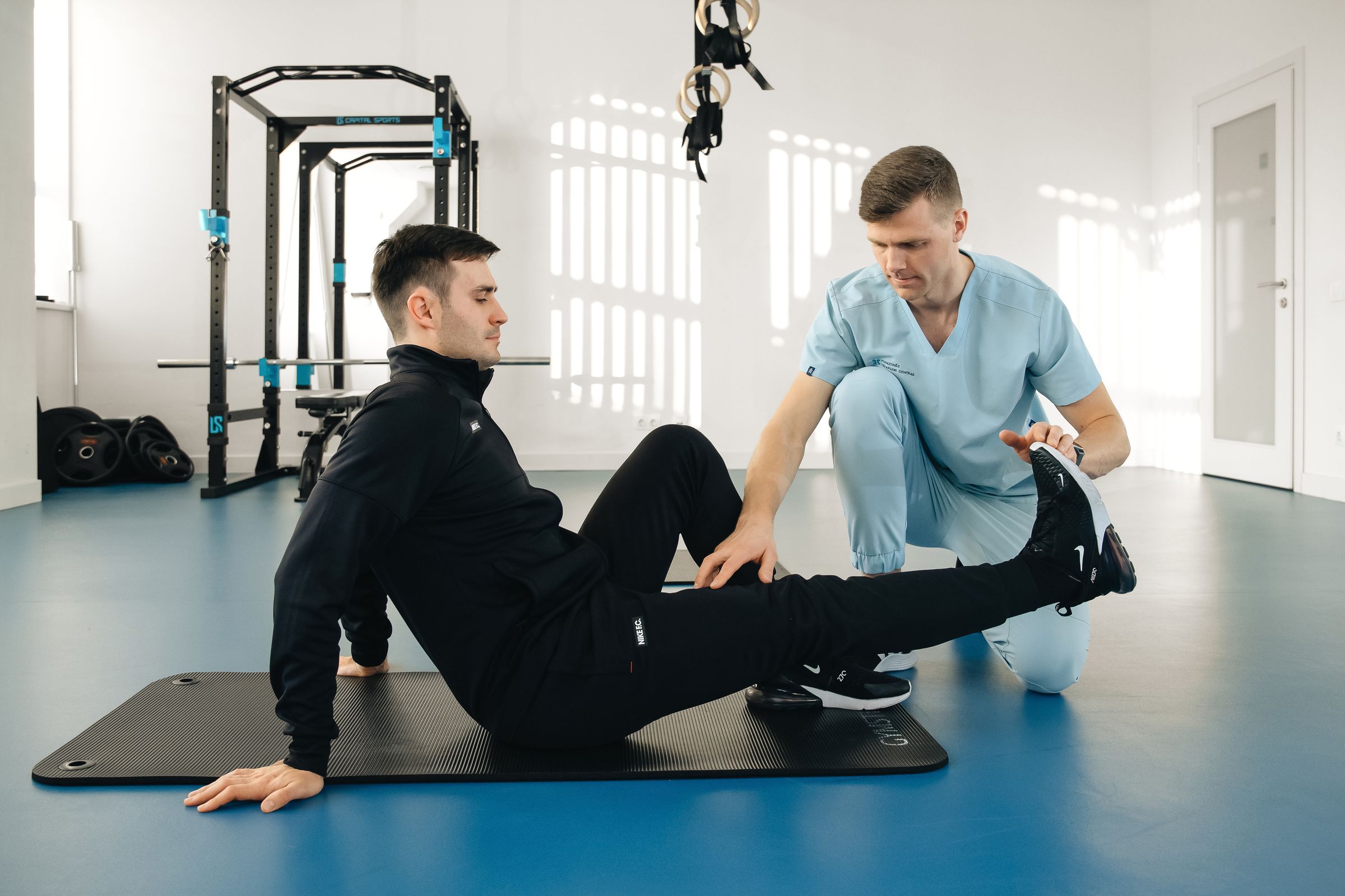 A physical therapist guiding a patient through a leg exercise on a mat