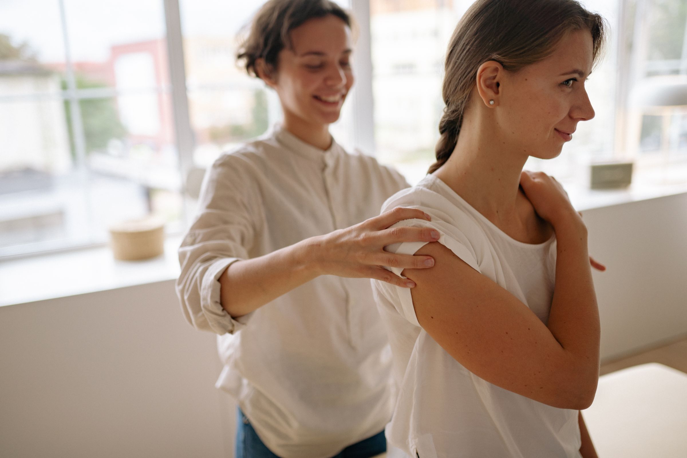 A smiling woman having her shoulder treated by a practitioner in a bright room