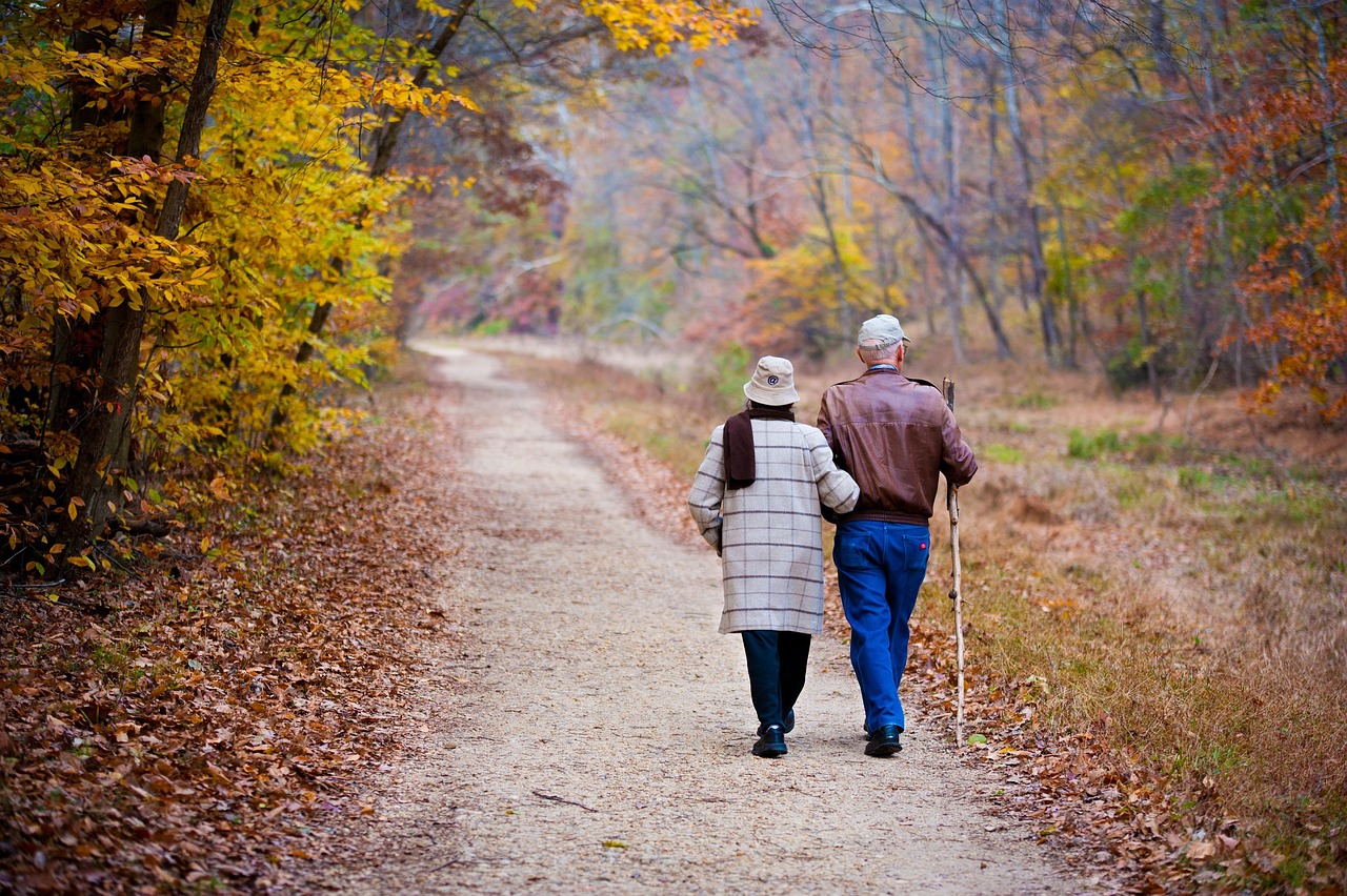 An older couple walking arm in arm on an autumn trail