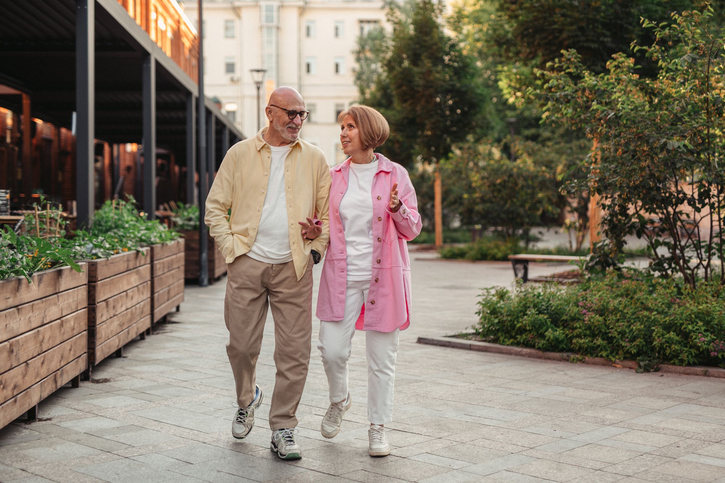 An older couple walking and talking on a leafy city street