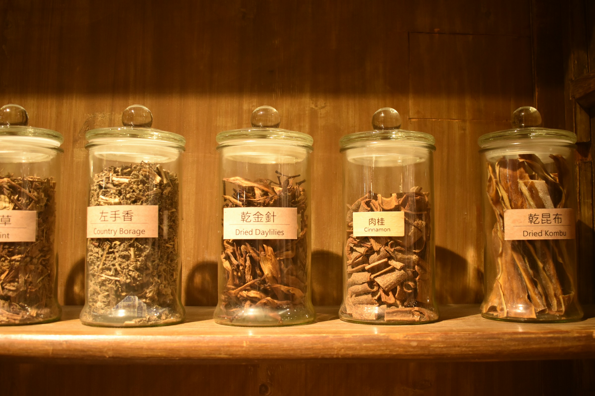Glass jars of dried herbs on a wooden shelf